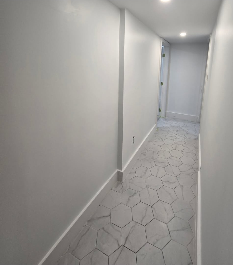 Long basement hallway with marble-look hexagonal tile flooring, fresh grey paint and recessed lighting