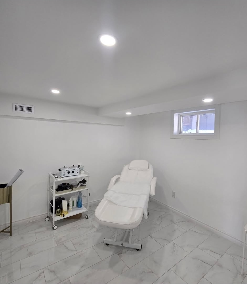 Bright basement treatment room with marble-look tile flooring, pot lights and egress window