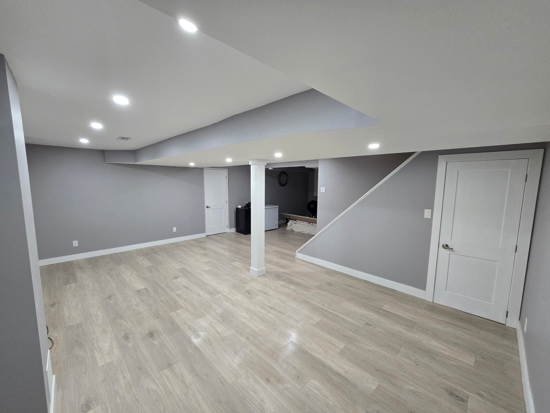 Finished basement living space with grey walls, pot lights and light vinyl plank flooring