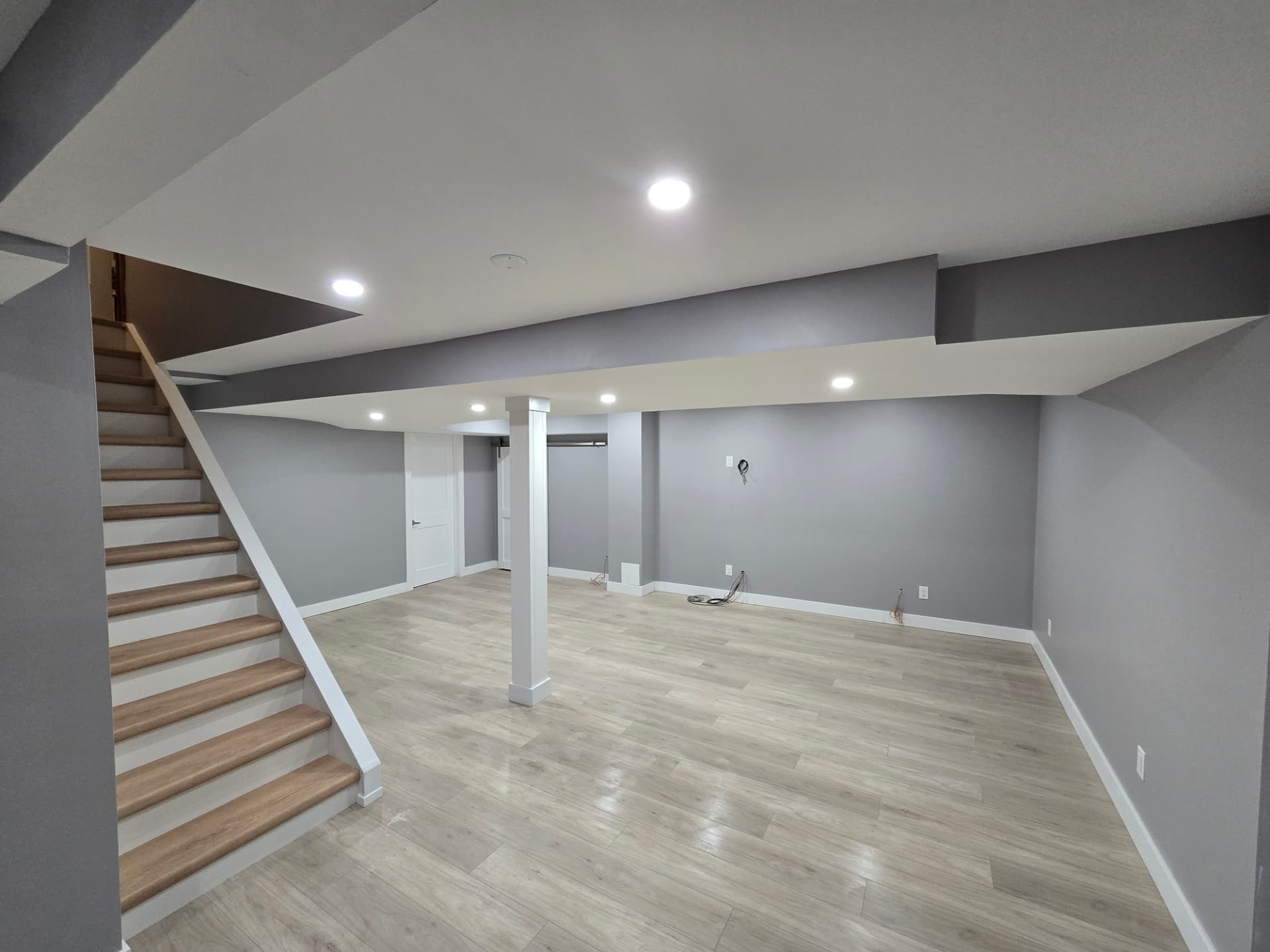 Finished basement with vinyl plank flooring, painted stairs and pot lights